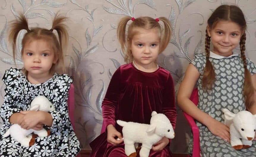 Three young girls in Ukraine holding lamb-shaped soft-toy speakers